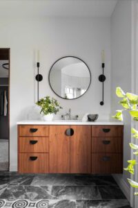 floating wooden vanity in bathroom with matte black hardware and round mirror