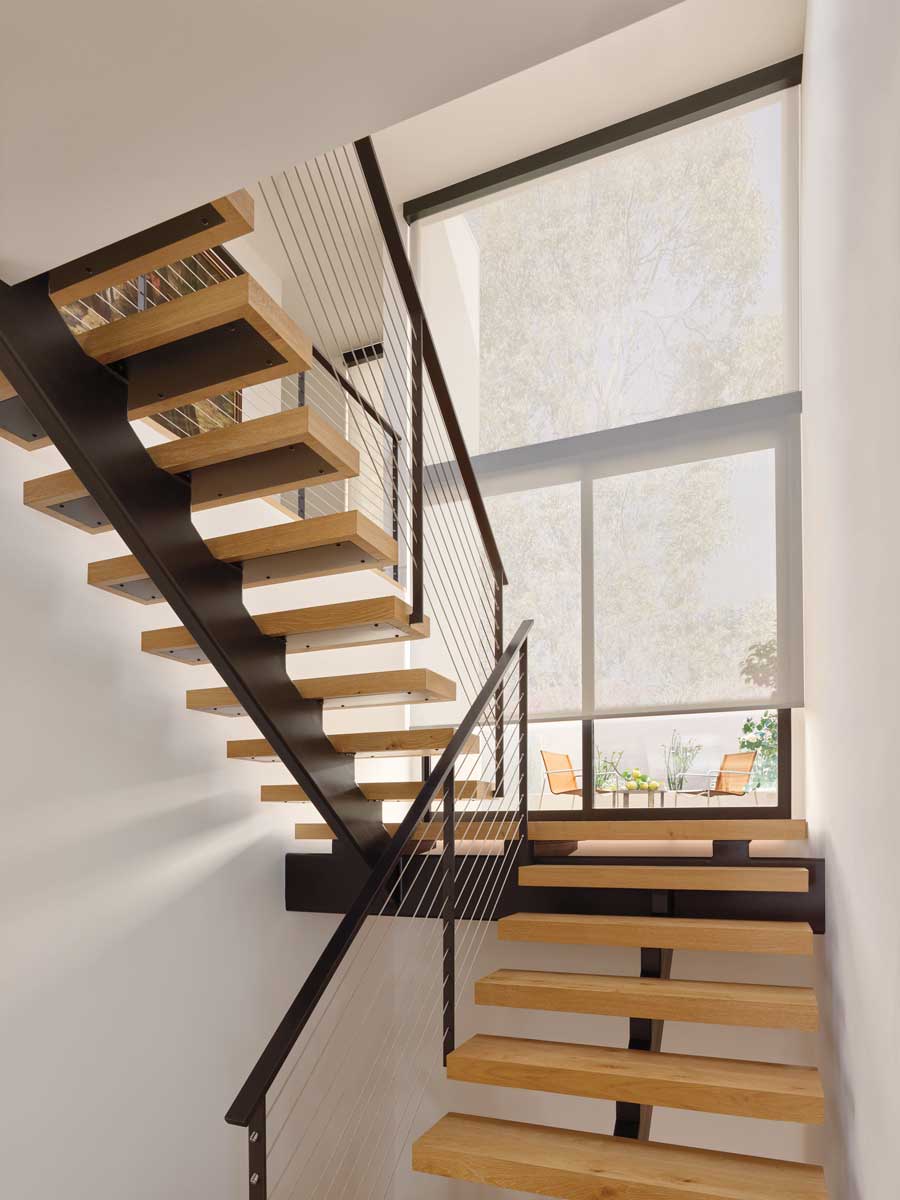 Wooden modern stairs with windows and roller shades on the landing between the stairs going up