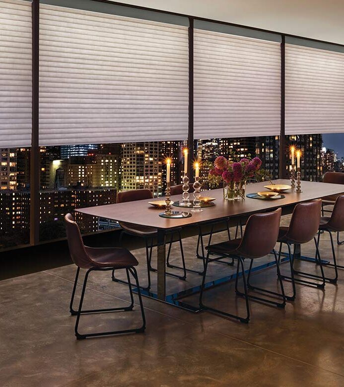 aura-illuminated-shades-cellular-roller-shades-hunter-douglas-timan-and-co a highrise apartment dining room space with large window shades by hunter douglas